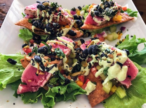 A plate of nachos topped with seared tuna, black beans, diced vegetables, and a creamy sauce on a bed of lettuce.