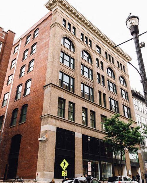 Historic brick building with large windows, featuring a mix of red and beige stone, located on a city street.