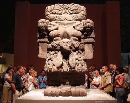 Visitors admire a large, intricately carved stone sculpture in a museum setting.