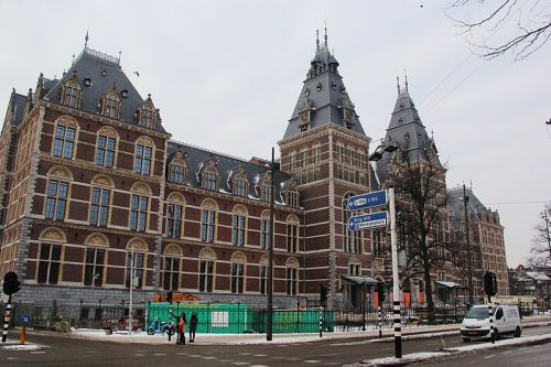 Historic building with ornate architecture, featuring towers and intricate brickwork, set against a cloudy sky.