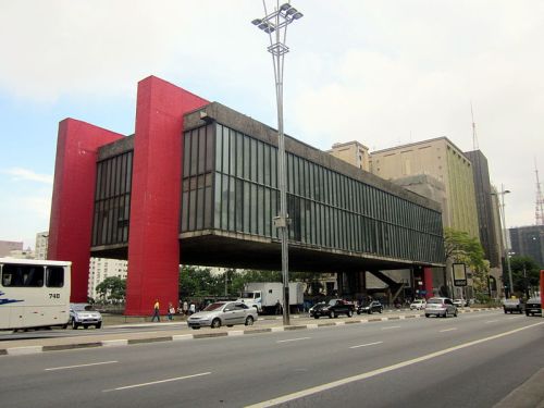 A modern building with a red and concrete structure elevated above a busy street, featuring large glass windows.