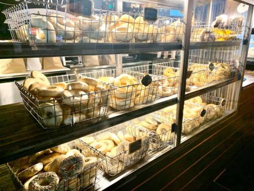 A display case filled with various types of bagels in wire baskets, illuminated warmly.