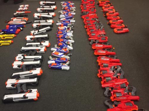 A collection of toy blasters arranged in rows, featuring various colors and designs on a carpeted floor.