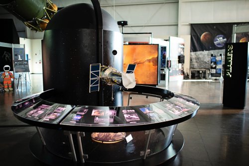 A space exhibit featuring a model satellite and informational displays about planets in a modern museum setting.
