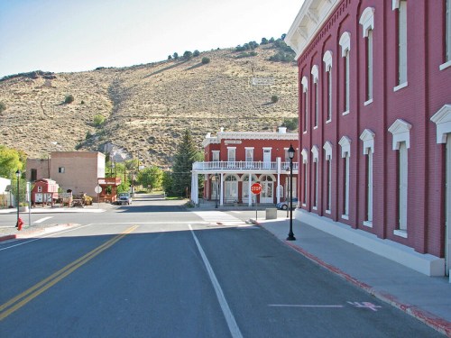 A quiet street scene with red brick buildings and a hillside in the background, featuring a stop sign and clear blue sky.