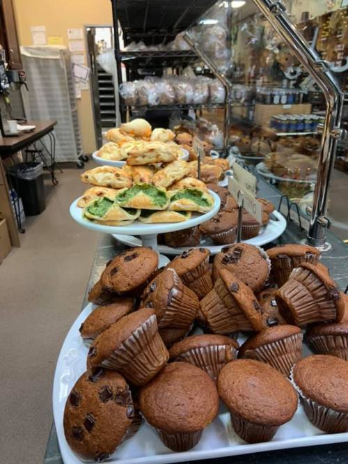 A display of assorted baked goods, including muffins and pastries, arranged on white plates in a bakery setting.