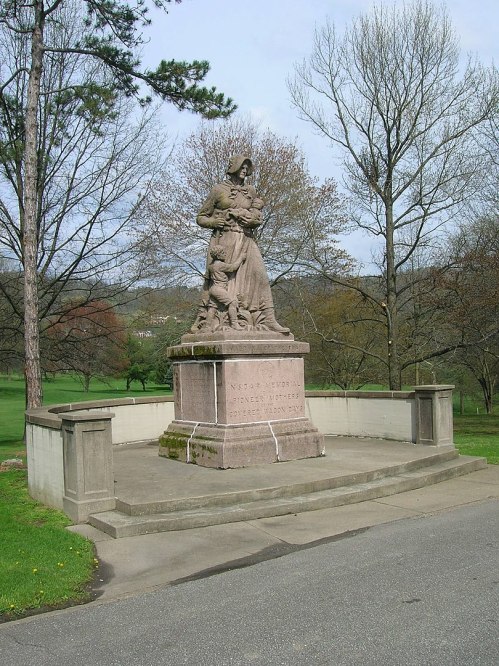 A stone monument featuring a woman holding children, surrounded by trees and a park-like setting.