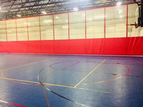 Indoor basketball court with blue flooring, red walls, and a basketball hoop in the corner.