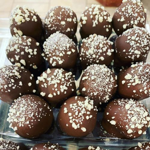 A close-up of chocolate truffles coated in nuts and sprinkled with powdered sugar, arranged in a clear container.