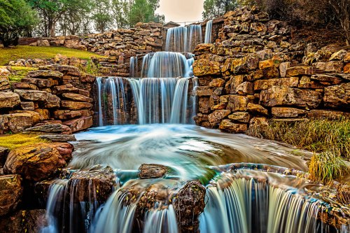 A serene waterfall cascading over rocky formations into a tranquil pool, surrounded by lush greenery.