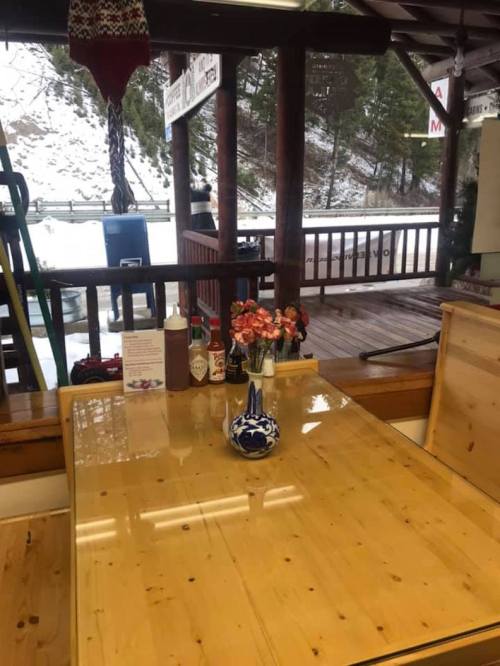 A wooden table with a vase of flowers, condiments, and a view of a snowy outdoor scene through a window.