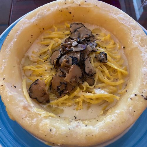 A creamy pasta dish served in a cheese wheel, topped with truffles and black pepper.