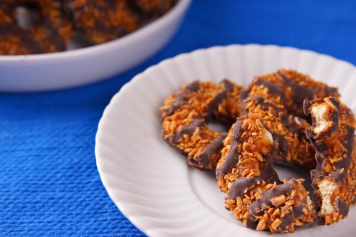A plate of chocolate-covered cookies with a coconut topping, set on a blue tablecloth.