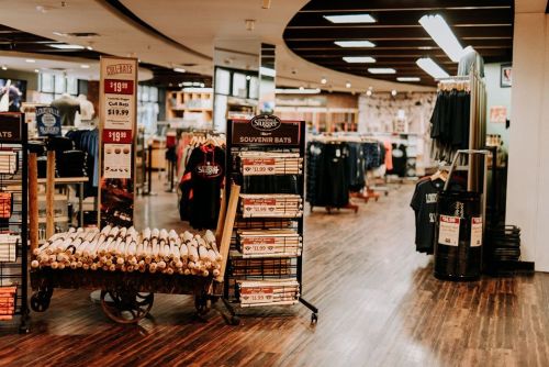 A retail store interior featuring souvenir bats, clothing racks, and a modern layout with wooden flooring.