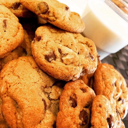 A close-up of freshly baked chocolate chip cookies stacked beside a glass of milk.