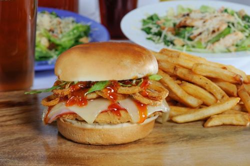A crispy chicken sandwich topped with lettuce, cheese, and sauce, served with a side of golden fries.