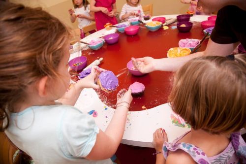 Children decorating cupcakes at a table, with colorful frosting and sprinkles scattered around.