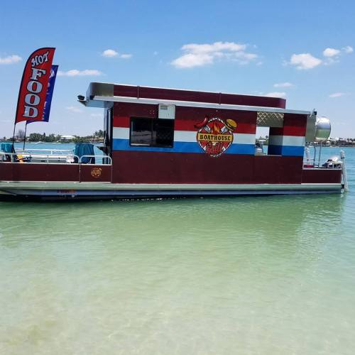 A colorful food boat with a "Boathouse" sign, floating on clear water under a blue sky with a "Hot Food" flag.