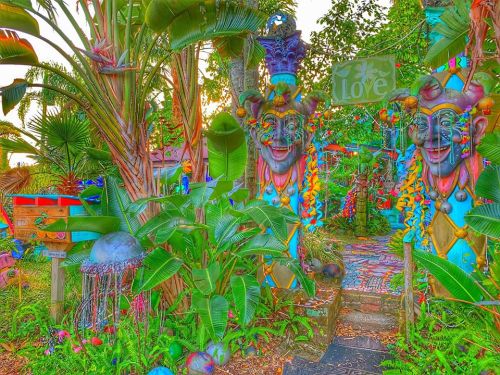 Colorful garden entrance with vibrant masks, lush greenery, and a sign reading "Love" amidst whimsical decorations.