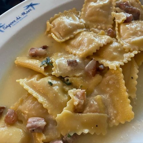 Plate of ravioli in a creamy sauce, garnished with small pieces of bacon and herbs.