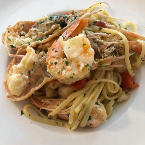 A plate of pasta with shrimp, lobster, and herbs, garnished with parsley and served with a light sauce.
