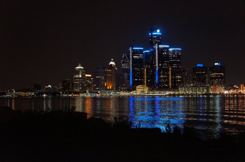 Night view of a city skyline with illuminated buildings reflecting on water.