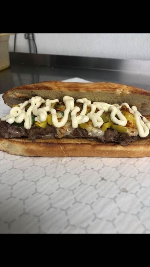 A sandwich filled with grilled beef, melted cheese, pickles, and drizzled with mayonnaise on a toasted bun.