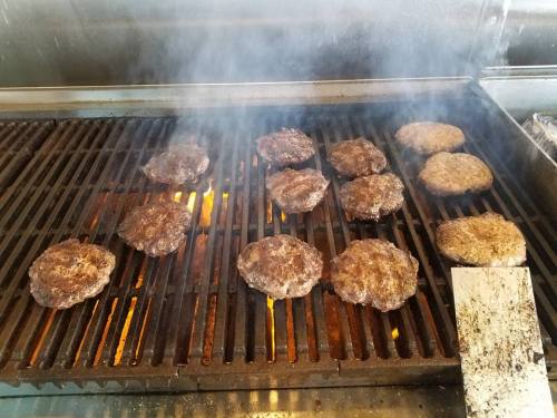Grilling burgers on a barbecue with smoke rising and flames visible beneath the grill.