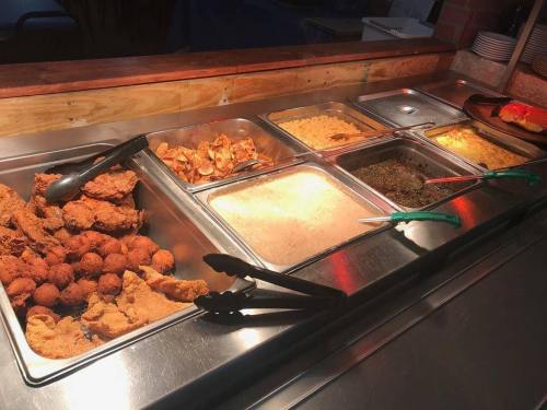 A buffet display with various dishes, including fried chicken, pasta, and sides, served in metal trays.