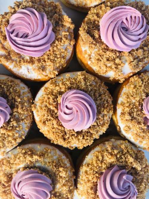 A close-up of donuts topped with purple swirled frosting and a crumbly topping, arranged in a neat pattern.
