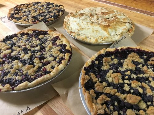 Four delicious pies on a wooden table: two berry pies with crumb topping and two with golden, flaky crusts.