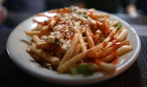A plate of French fries topped with cheese, green onions, and drizzled with ketchup.