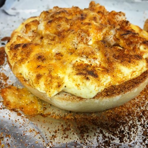 A baked dish in a bread bowl, topped with melted cheese and spices, resting on a parchment-lined surface.