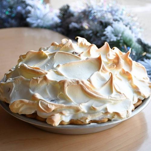 A beautifully baked meringue pie with golden peaks, set on a wooden table with festive decorations in the background.