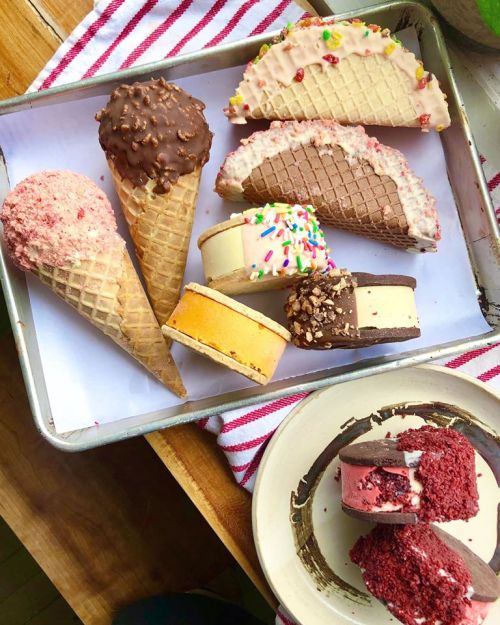 A tray of various ice cream cones and sandwiches, including chocolate-dipped and colorful sprinkles, on a striped cloth.