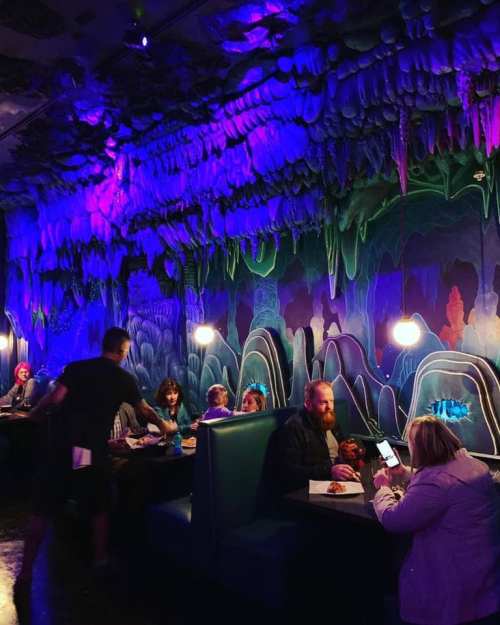 A vibrant restaurant interior with colorful, cave-like decor and patrons dining at booths under soft lighting.