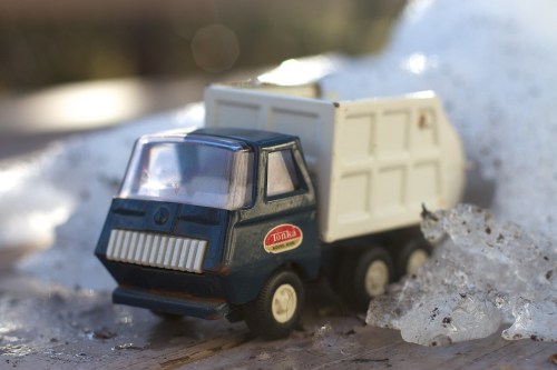 A vintage blue Tonka toy dump truck on a wooden surface with ice and snow in the background.