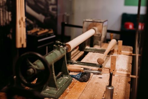 A woodworking lathe with wooden pieces and shavings on a workbench in a workshop setting.