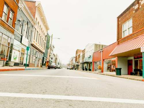 A quiet street scene featuring historic buildings, shops, and a car parked along the curb under a cloudy sky.