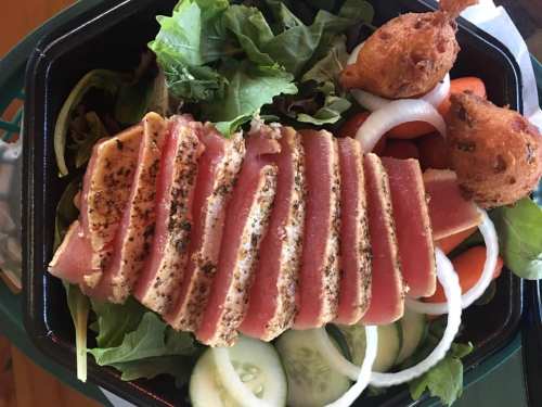 A salad with sliced seared tuna, mixed greens, cucumbers, onions, carrots, and two fried items on the side.