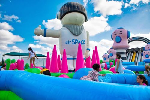 A colorful inflatable playground with a giant astronaut figure and children playing among pink and blue structures.