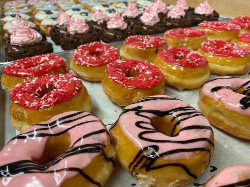 A variety of colorful donuts with pink, red, and chocolate icing, topped with sprinkles, arranged on a tray.