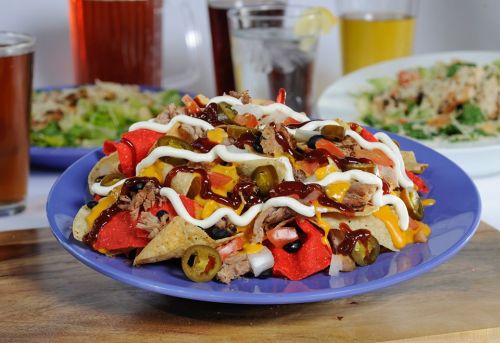 A colorful plate of nachos topped with cheese, barbecue sauce, jalapeños, and drizzled with mayonnaise.