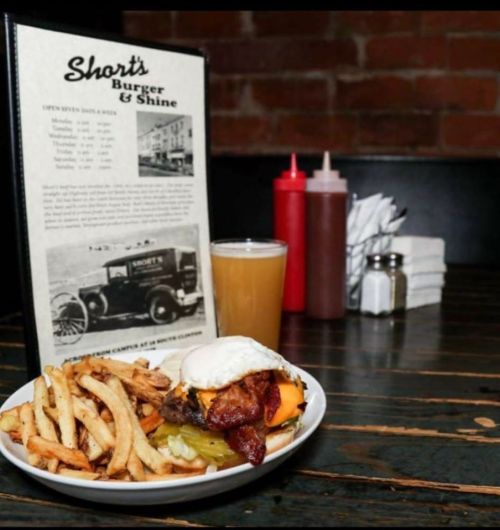 A burger with bacon and cheese, fries, and a drink on a table with a menu in a cozy restaurant setting.