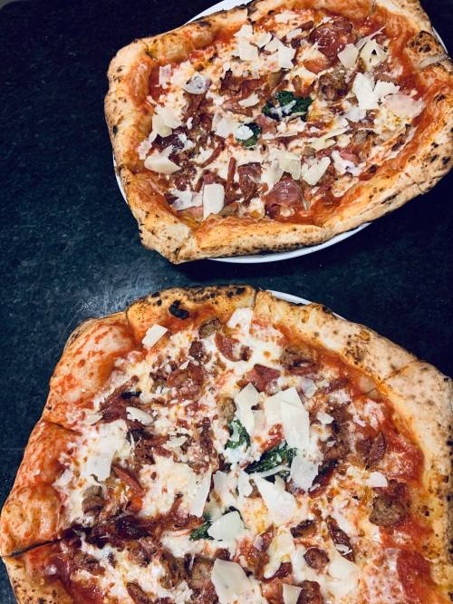 Two pizzas on a dark surface, topped with cheese, pepperoni, and herbs, with a crispy crust.