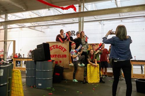 A group of people posing with toy blasters at the Detroit Art Club, surrounded by colorful foam darts and playful decor.