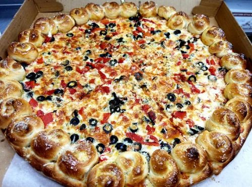 A large pizza with a stuffed crust, topped with cheese, olives, and red peppers, in a pizza box.