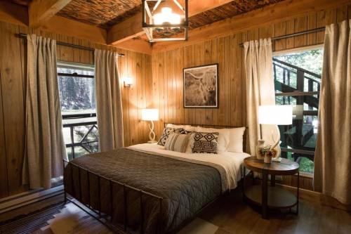 Cozy wooden bedroom with a queen bed, two lamps, and large windows overlooking greenery.