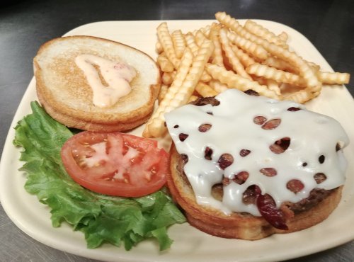 A plate with a burger topped with melted cheese, lettuce, tomato, and crinkle-cut fries on the side.