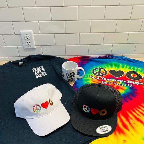 A collection of merchandise featuring a black shirt, white hat, black hat, mug, and a colorful tie-dye shirt.
